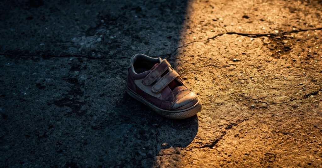A worn child's shoe resting at the threshold of shadow and light. Featured image for the poem The Children We Once Were on Sayspire.