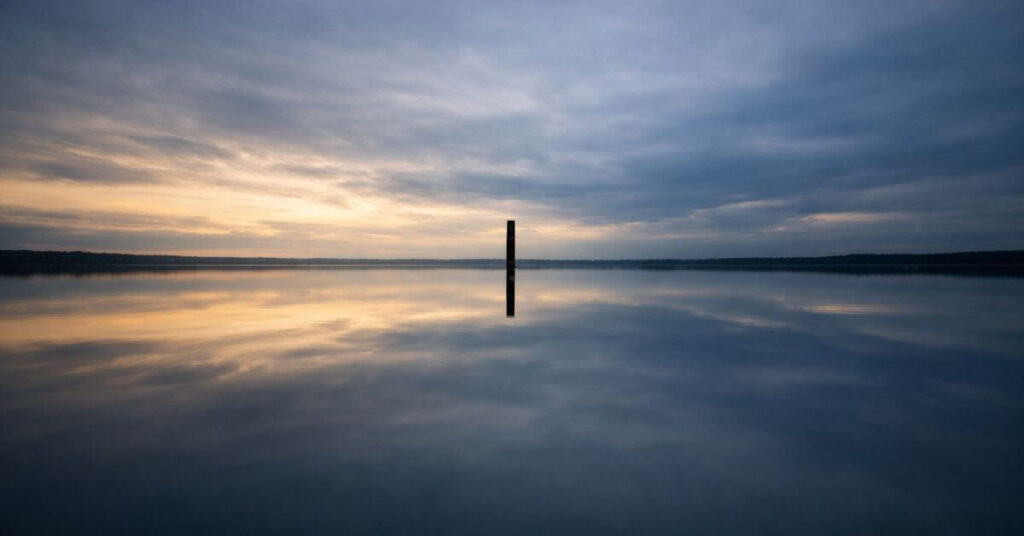 A glassy lake reflecting the open sky at dusk. Featured image for the poem At Week's End on Sayspire.