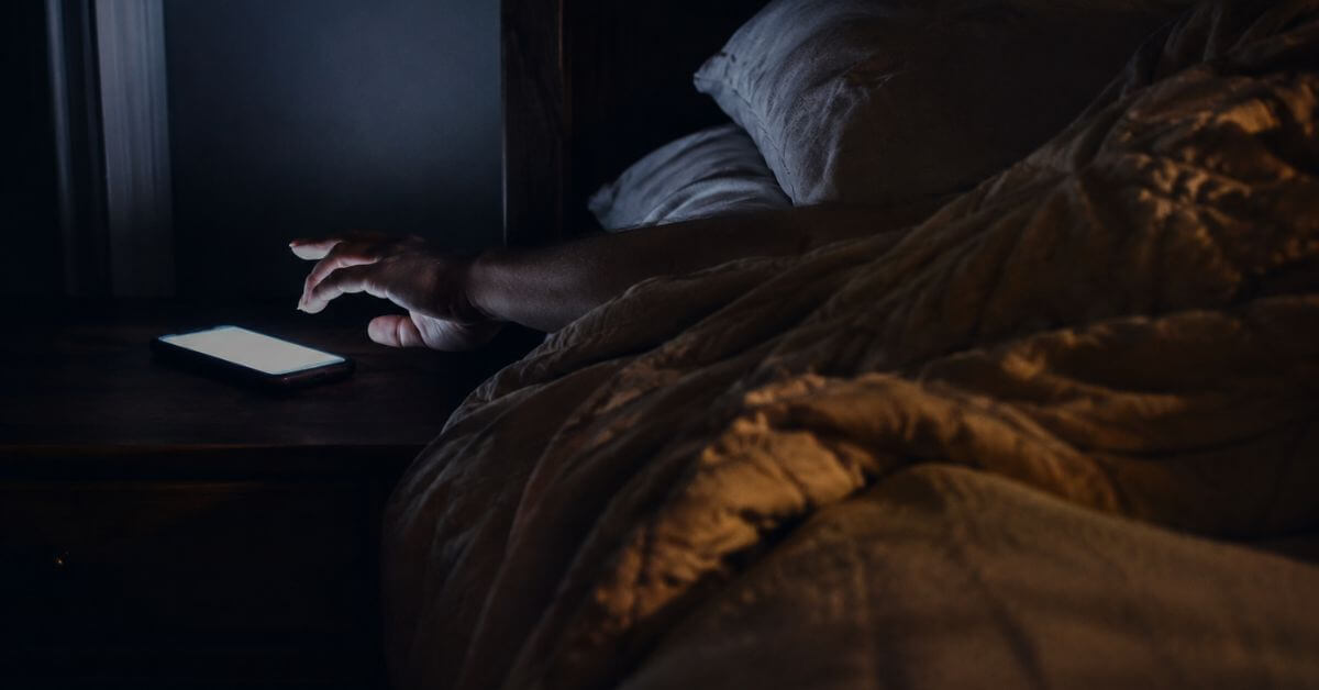 A dim bedroom in pre-dawn stillness, a glowing iPhone on a nightstand illuminating an outstretched arm; featured image for the poem Ten Sacred Minutes on Sayspire.