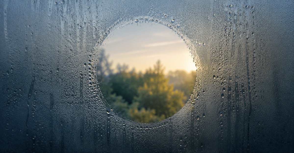 A clear circle wiped into a fogged window, morning light blurring beyond, a poem about feeling alive by Joshua Cintron.